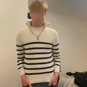 Randig half zip tröja från Zara - Snygg stickad tröja från Zara i beige med mörkblå horisontella ränder. Tröjan har en half zip-dragkedja vid kragen och långa ärmar. Perfekt för dig som gillar en klassisk och chill stil.