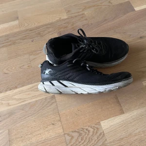 Svarta löparskor från Hoka One One - Hoka One Clifton 6 Säljer ett par begagnade Hoka One Clifton 6 löparskor i svart/vitt. Storlek EU 41 1/3. Skorna är använda (se bilder) men fungerar fortfarande bra som träningsskor.  Använda i 2 år. Köpta på Löplabbet, nypris: 1.900 kr.  skickas mot att köparen betalar frakten.  Skicka gärna ett meddelande vid intresse eller frågor!