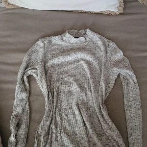 Gråmelerad polotröja från Vero Moda 💗 - Säljer en gråmelerad polotröja från Vero Moda i mjukt ribbat material. Tröjan har lång ärm och en högre krage som ger en clean och stilren look. Perfekt att styla med jeans eller kjol för en chill vibe.