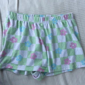 Blommiga rutiga pyjamas shorts från Primark - Söta shorts från Primark med grönt och vitt rutmönster och blommor i pastellrosa och ljusblått. Mjuk resår i midjan och avslappnad passform. Perfekta för varma dagar och chill hemma. Tillverkade i bomull för en skön känsla.