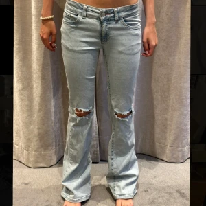 Ljusblå bootcut jeans med slitningar - Snygga ljusblå jeans med bootcut passform och slitna hål på knäna. Jeansen har klassisk femficksdesign och broderade detaljer på bakfickorna. Perfekta för dig som gillar en avslappnad och trendig stil.Midjemått: 33cm tvärsöver(stretchiga), innerben: 83 cm