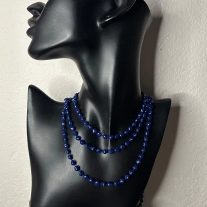 Långt retrohalsband med oregelbundna koboltblå pärlor 130 cm Vintage 70-tal  - Långt retrohalsband från 70-talet, inropat på auktion med äldre bijouterier. Halsbandet är ca 130 cm långt och kan bäras enkelt, dubbelt eller trippelt för olika uttryck.  De oregelbundet formade pärlorna i intensiv koboltblå färg har en blank glans som ger halsbandet ett elegant men ändå lekfullt utseende. Materialet är akryl/plast, typiskt för epoken, och gör smycket lätt och bekvämt att bära.  Jag prutar inte men erbjuder rabatt vid köp av flera saker. 