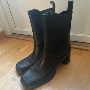Svarta Vagabond boots - Använd sen gång! Snygga svarta chelsea boots i skinn med fyrkantig tå och bred klack. Skorna har elastiska paneler på sidorna och dragflikar upptill för enkel påtagning. Perfekta för dig som gillar en stilren och edgy look.