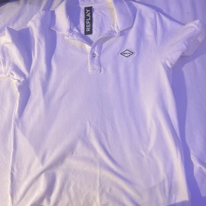 Aldrig använ Vit pikétröja från Replay, stl S - Klassisk vit pikétröja från Replay i storlek S. Tröjan har korta ärmar, krage och knäppning framtill samt Replay-logga på bröstet. Tillverkad i mjuk bomull som känns skön mot huden. Perfekt för en clean och stilren look.