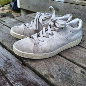 Ljusgrå sneakers från Björn Borg - Snygga ljusgrå sneakers från Björn Borg med klassisk design. Stl 39. Skorna har ovandel i mocka och detaljer i vitt syntet, rund tå och platt sula. Tjocka snören och diskreta perforeringar på sidorna ger en clean look. Perfekta för dig som gillar stilrena och enkla sneakers. De är slitna  I häl, sulaoch en gräsfläck på ovansidan, syns på bilderna