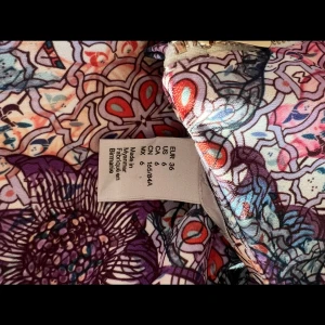 Färgglad blommig ärmlös klänning - Säljer en superfin ärmlös klänning med färgstarkt blommigt mönster i lila, rosa, blått och rött. Klänningen har rund halsringning, dragkedja bak och figurnära passform. Perfekt för dig som vill sticka ut med en unik look!