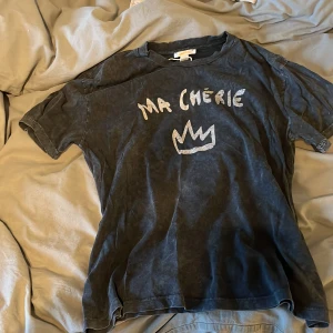 Svart t-shirt Ma Chérie Gina Tricot - Cool svart t-shirt från Gina Tricot med vit text 'Ma Chérie' och en krona på bröstet. T-shirten har tvättad look, rund hals och korta ärmar. Perfekt för en avslappnad och trendig stil.