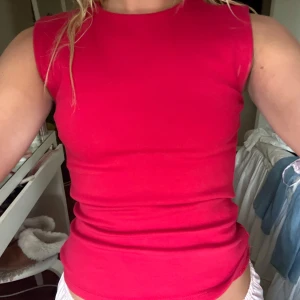 Röd ärmlös linnetopp - Snygg röd ärmlös linnetopp i stretchigt material. Enkel och stilren design med rund halsringning, perfekt att matcha med jeans eller kjol. Passformen är tight och toppen är superbekväm för varma dagar.