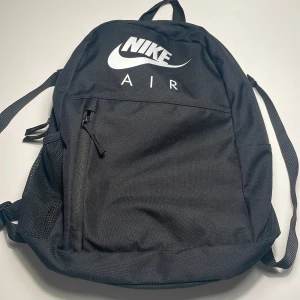 Svart Nike Air ryggsäck - Säljer en svart ryggsäck från Nike Air med vit logga framtill. Väskan har justerbara axelremmar, ett stort huvudfack, framficka med dragkedja och sidoficka i mesh. 