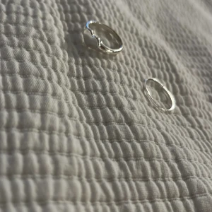 Två silverringar med unik design - Säljer två stilrena silverringar. Ena ringen har en vågig, organisk form som ger en cool och modern vibe, medan den andra är tunn och minimalistisk. Perfekta att bära tillsammans eller var för sig för en trendig look.