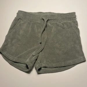 Gröna frottéshorts XOX Friends - Mysiga göna shorts från XOX Friends i mjuk frotté. De har elastisk midja med snörning och två fickor framtill. Perfekta för chill dagar eller när du vill ha något bekvämt och enkelt. Klassisk modell med loose fit och sköna material. Storlek 146/152 