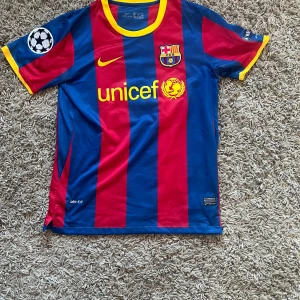 FC Barcelona Messi 10 Nike matchtröja - Säljer en ikonisk FC Barcelona matchtröja med Messi 10 på ryggen. Tröjan är kortärmad, har breda blå och röda ränder, gula detaljer och klubbmärke på bröstet. Tillverkad i lätt och ventilerande Dri-FIT-material. Perfekt för dig som älskar fotboll och Barca. 
