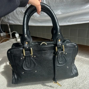 Chloé Paddington  - Saljer min alskade Chloé Paddington väska som är i bra skick. Jag har lagt i ett inlägg i den som ger den mer struktur vilket ingår om man vill. Bild 4 är utan inlägget. Den har några skador pả insidan av väskan och tyvärr saknar den låset. Saknar även två nitar under väskan.  Skriv om du har frågor eller vill ha fler bilder. Priset är förhandlingsbart! Mått: Längd 33 cm Höjd ca 18 cm Djup ca 15 cm