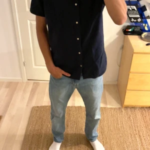 Mörkblå kortärmad skjorta Jack & Jones - Snygg mörkblå skjorta från Jack & Jones i bomull. Skjortan har korta ärmar, klassisk krage med knappar och vita knappar längs hela framsidan. Perfekt för en clean och stilren look.