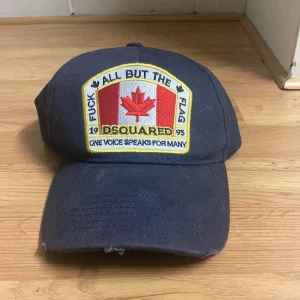 Blå keps från Dsquared med patch - Blå keps från Dsquared med stor broderad patch framtill som har Kanadas flagga och text. Böjd skärm och justerbar baksida. Snygg streetstil med tydlig logga och detaljer i rött, vitt och gult. Hör av er om ni har några frågor! 