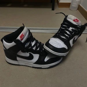 Nike Dunk High svart/vit 38.5 - Säljer ett par Nike Dunk High sneakers i svart och vitt skinn med klassisk röd Nike-logga på plösen. Använda ett fåtal gånger