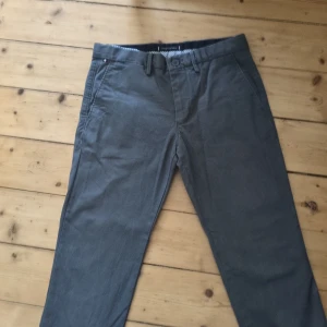 Grå chinos från Tommy Hilfiger 30/32 - Snygga grå chinos från Tommy Hilfiger i klassisk rak modell. Byxorna har sidfickor, bakfickor med knapp och bälteshällor. Perfekta för en clean och stilren look. Tillverkade i mjuk bomull för skön känsla hela dagen.