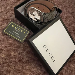 Gucci bälte - Snyggt Gucci-bälte med klassiskt GG mönster i beige och grå toner. Bältet har en stor, rund silverspänne med GG-logga och är gjort i skinn med canvas-yttersida. Perfekt accessoar för att lyfta din outfit med en lyxig touch. Priset går att diskuteras.