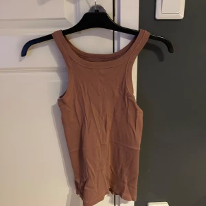 Brun ribbad linnetopp från 157 - Säljer en brun ribbad linnetopp från 157 i storlek S. Toppen är ärmlös med breda axelband och rundad halsringning. Tillverkad i 100% bomull för en skön och mjuk känsla. Perfekt att styla med jeans eller kjol för en enkel och snygg look.