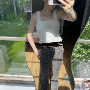 Vit smockad linnetopp från H&M Divided - Supersöt vit linnetopp från H&M Divided med smockad resår över hela toppen och breda axelband med volangdetaljer. Tunt bomullstyg med små broderade hål för extra sommarkänsla. Perfekt till jeans eller kjol när det är varmt ute.