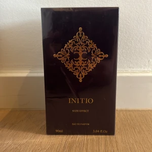 Initio Side Effect Eau de Parfum 90ml - Initio Side Effect Eau de Parfum i lyxig mörklila kartong med gulddetaljer och elegant mönster framtill. Flaskan rymmer 90 ml och är tillverkad i Frankrike. En exklusiv parfym som utstrålar mystik och elegans.