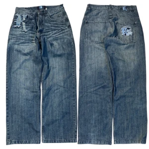 Baggy jeans från Karl Kani med brodyr - Säljer ett par blå baggy jeans från Karl Kani med stora broderade K-loggor i blått och svart framtill och på bakfickan. Jeansen har bred passform, klassisk femficksdesign och cool streetwear-vibe. Perfekta för dig som gillar oversized och statement-plagg.