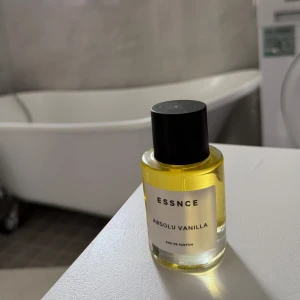 ESSNCE Absolu Vanilla parfym - Helt oanvänd då jag råkade beställa två st.                        En stilren parfymflaska från ESSNCE med doften Absolu Vanilla. Flaskan är cylindrisk i genomskinligt glas med guldfärgad vätska och svart rund kork. Minimalistisk etikett framtill. Perfekt för dig som älskar varma, söta vaniljtoner.