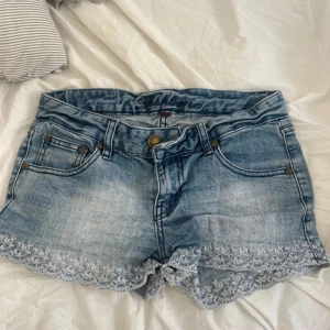 Jeansshorts med spets från fishbone - Snygga ljusblå jeansshorts från fishbone med dekorativ vit spetskant längst ner. Klassisk femficksmodell med knapp och dragkedja framtill. Perfekta för sommardagar när du vill ha en söt men avslappnad look.