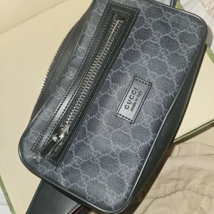 Svart Gucci axelväska med GG-mönster - Säljer en original svart axelväska från Gucci med klassiskt GG-mönster i grått. Väskan har justerbar axelrem i rött och marinblått, silverfärgade dragkedjor och detaljer i skinn. Väskan är i nyskick, använd kanske 3 gånger. Kvitto finns. Pris i en gucci butik är ca 13 tusen kr. Mitt pris kan diskuteras vid snabb affär