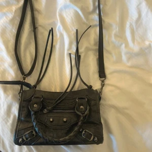 Citybag - Cool svart Citybag i skinn med klassiska detaljer som flätat handtag, silverfärgade nitar och dragkedja framtill. Väskan har långa läderband och justerbar axelrem, perfekt för att bära crossbody, går även att ta av om man inte vill ha axelrem. Snygg och edgy design som lyfter varje outfit. Köpt här på plick men kommer tyvärr inte till användning!💕💕💕