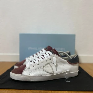 Philippe Model sneakers - Snygga Philippe Model sneakers i vitt skinn med vinröda mockadetaljer på tå och plös samt mörkblå häl. Klassisk låg modell med vita snören och rund tå. Perfekta för dig som gillar stilrena men ändå unika sneakers. Bra skick! Riktigt snygga och sällsynta med ett nypris på 6500 kr!!! Skriv för frågor! Perfekta inför sommaren!!! 🥰😍
