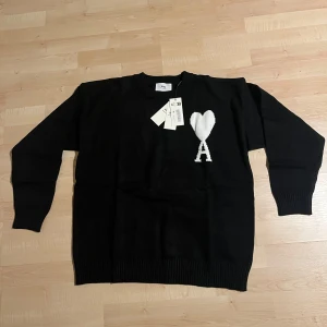 Svart stickad tröja från Ami Paris - Svart stickad tröja från Ami Paris med rund hals och lång ärm. På bröstet finns ett vitt hjärta och bokstaven A. Tröjan har ribbade muddar och en klassisk passform som funkar till många stilar. Oanvänd, pris kan diskuteras 