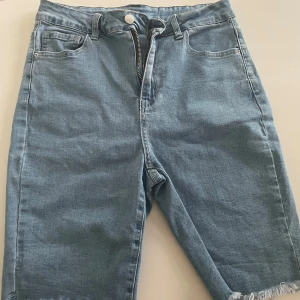 Ljusblå jeansshorts med rå kant - Snygga ljusblå jeansshorts med klassisk femficksdesign och rå, fransad kant nedtill. Modellen har hög midja och dragkedja framtill. Perfekta för en chill sommardag och lätta att matcha med allt. L men funkar som M ( liten i storlek )