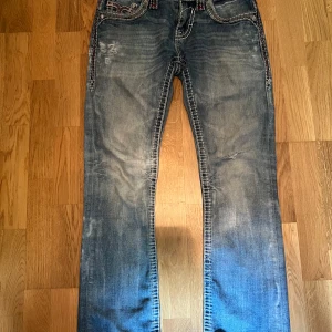 Jett rock revival - Snygga blå jeans från Jett i modellen Slim Boot med coola kontrastsömmar och broderade detaljer på fickorna. Jeansen har en klassisk bootcut-passform och slitna partier för en trendig look. Det finns ett litet hål i grenen som inte märks av när man har på sig dom