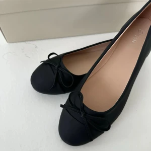 Svarta ballerinaskor med rosett -  svarta ballerinaskor med rund tå och söt rosettdetalj framtill. Skorna har en platt sula och är tillverkade i ett matt material som ger en stilren look. Perfekta att matcha med både jeans och kjol för en enkel och snygg outfit, aldrig använda 🌸