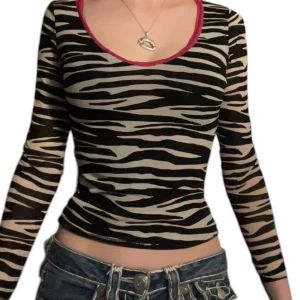 Zebramönstrad topp från Phard - Säljer en snygg zebramönstrad topp från Phard. Den har en v-ringad design med rosa spetsdetaljer runt halsen. Toppen är långärmad och har en tight passform.