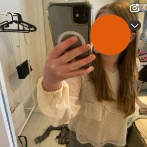 Ljusbeige blus med volang och prickar - Säljer en söt ljusbeige blus med volangdetaljer och diskret prickigt mönster. Blusen har långa, luftiga ärmar med resår vid handlederna och en lätt transparent känsla. Perfekt för dig som gillar romantisk och trendig stil.