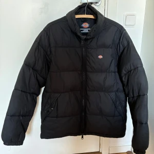 Dickiesjacka - Svart pufferjacka från Dickies i storlek large. Passar dock mig som är medium perfekt. Jackan har en clean look med Dickies-logga på bröstet, hög krage och dragkedja framtill. Perfekt för kalla dagar med sin vadderade design. Nypris är ca 1200kr. Tveka inte att skriva om du har frågor!😊 