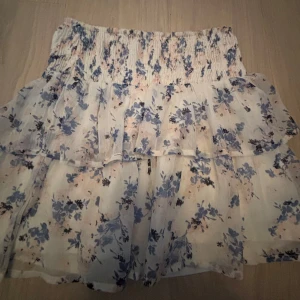 Blommig volangkjol från Vero Moda - Supersöt kort volangkjol från Vero Moda i vitt med blått och ljusrosa blommönster. Kjolen är i storlek XS. 