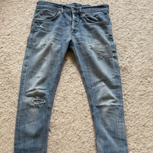 DONDUP JEANS - Säljer ett par blå jeans från ERT i storlek 30. Jeansen har slitna detaljer och hål på benen för en cool, avslappnad look. Klassisk femficksmodell med normal passform och dragkedja. Perfekta för dig som gillar en streetstyle vibe. DM FÖR FÅRGOR!🙌