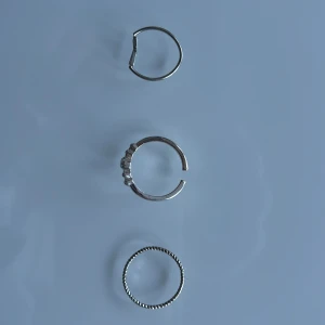 3-pack silverfärgade minimalistiska ringar - Säljer tre tunna ringar i silverfärg. En ring har tvinnad design, en är öppen med små kulor och en är öppen med två små trianglar. Perfekta för att mixa och matcha för en stilren look. Två av dom är justerbara. Helt ny. Mycket bra.