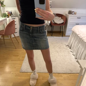 Klassisk jeanskjol i kort modell - Säljer en snygg kort jeanskjol i klassisk blå denim med slitna detaljer och femficksdesign. Kjolen har normal passform, bälteshällor och dragkedja framtill. Säljer då den var lite för stor💕