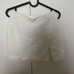 Vit kortkjol med slits framtill - Snygg vit kortkjol i enkel design med en liten slits framtill. Lågmidjad.