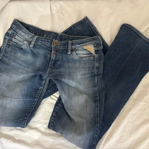 Replay bootcut jeans - Snygga blå bootcut jeans från Replay med låg midja och broderade detaljer på bakfickorna. Jeansen har en vanlig femficksmodell. Jag har lämnat in jeansen hos en sömmerska för att förstärka dom vid grenen eftersom det var lite slitet där.     Innerbenslängd: 78cm, Midja rakt över: 37cm. 