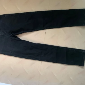 Svarta Levi's 502 jeans W30 L34 - Svarta jeans från Levi's modell 502 med klassisk femficksdesign och rakt snitt i storlek W30/L34. Jeansen har normal passform och är tillverkade i slitstarkt denimtyg. Perfekta för dig som gillar en clean, vädrad och tidlös look. 