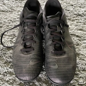 Svarta Nike Mercurial fotbollsskor - Säljer ett par svarta Nike Mercurial fotbollsskor med snörning och mönstrad ovandel. Skorna har rund tå, platt sula med dobbar för bra grepp på planen och är tillverkade i syntetmaterial. Snygg, diskret design med Nike-logga på sidan. De var dyra nya men på fjärde bilden så är de lite skadade därav priset, men fullt fungerande. Går säkert och laga också! Kan medge att de är lite små i storleken också. Pris ej hugget i sten.