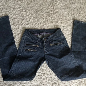 Mörkblå jeans med dragkedjedetaljer JC - Snygga mörkblå jeans från JC med flera dragkedjor framtill och baktill som cool detalj. Jeansen har en klassisk femficksmodell och är tillverkade i stretchigt denim för skön passform. Perfekta för dig som gillar en edgy stil.