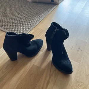 Svarta stövletter från Mango - Snygga svarta stövletter från Mango med klack och dragkedja på sidan. Skorna har spetsig tå och är gjorda i mocka med en stilren look. Perfekta för dig som vill ha en trendig och tidlös sko med lite edge.