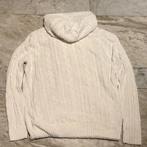 Vit stickad tröja från Ralph Lauren - Säljer en sjukt mysig vit stickad kofta från Polo Ralph Lauren. Koftan har huva med skönt foder, bruna knappar och klassiskt kabelstickat mönster. Storlek L men skulle säga att den passar mer medium. Hör av er för frågor!