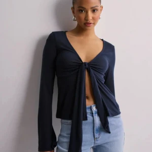 Mörkblå långärmad knytblus - Snygg mörkblå långärmad blus med djup v-ringning och knyt framtill. Modellen är croppad och har en mjuk, följsam passform. Perfekt att styla med jeans för en trendig look.